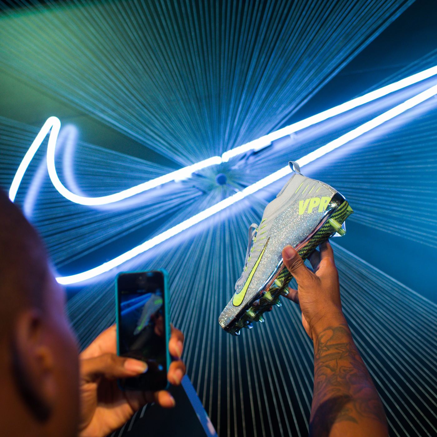 Athlete photographing a Nike cleat under a neon swoosh